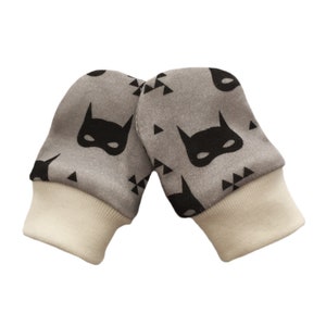 May include: A pair of gray baby mittens with a black and white geometric pattern and a black batman mask design.
