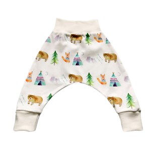 May include: White baby pants with a woodland animal print featuring bears, foxes, and teepees. The pants have a cream colored waistband and cuffs.
