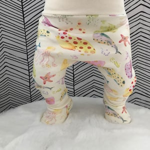 May include: White baby pants with a colorful sea life print. The print features fish, starfish, and coral.