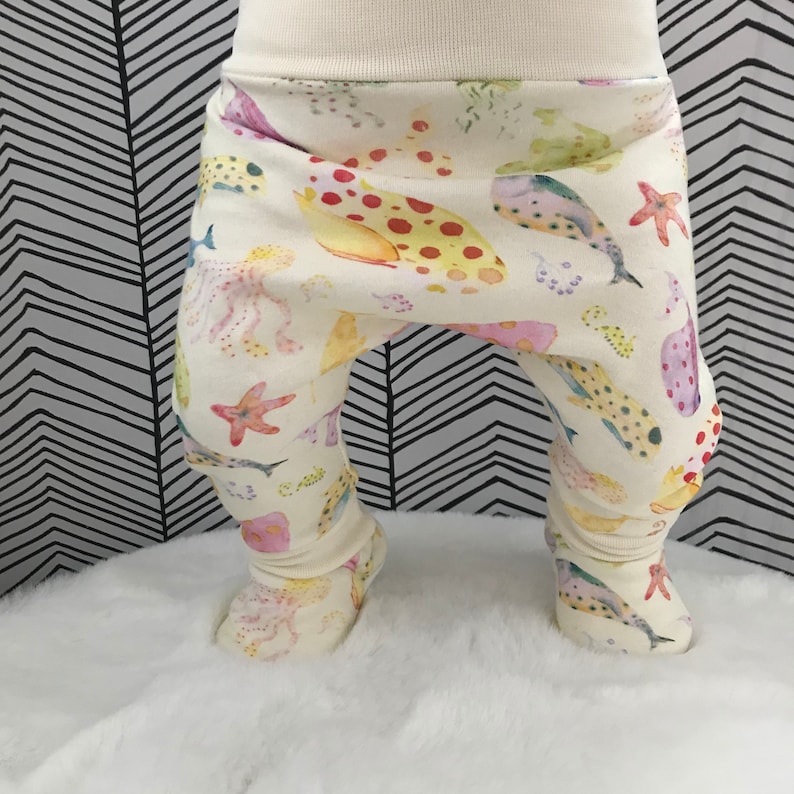 May include: White baby pants with a colorful sea life print. The print features fish, starfish, and coral.