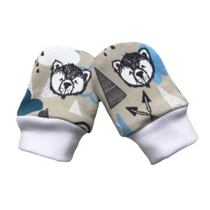 May include: A pair of baby mittens with a beige background and a white cuff. The mittens feature a repeating pattern of black and white bear faces, blue and gray triangles, and blue clouds.