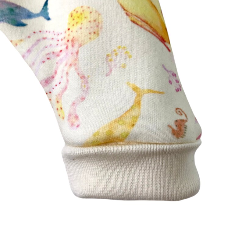 May include: Close-up of the cuff of a white long-sleeved shirt with a colorful sea creature print. The cuff is folded over and shows the white fabric underneath.