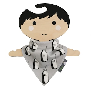 Puede incluir: Un bandana gris con un estampado de botella de leche en blanco y negro. El bandana está colgado en una percha de madera con forma de muñeca.