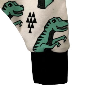 May include: White fabric with a black cuff and a repeating pattern of green dinosaurs and black triangles.