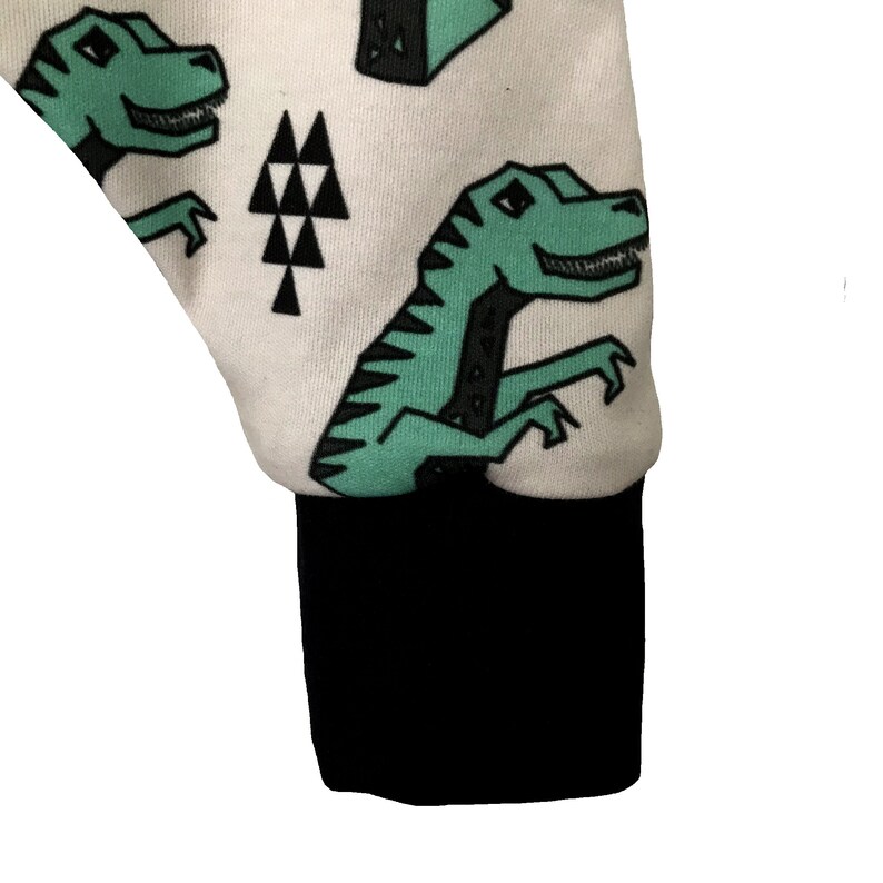 May include: White fabric with a black cuff and a repeating pattern of green dinosaurs and black triangles.