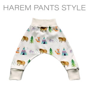 May include: White harem pants with a whimsical woodland print featuring bears, foxes, and teepees. The print is in shades of blue, green, orange, and purple.