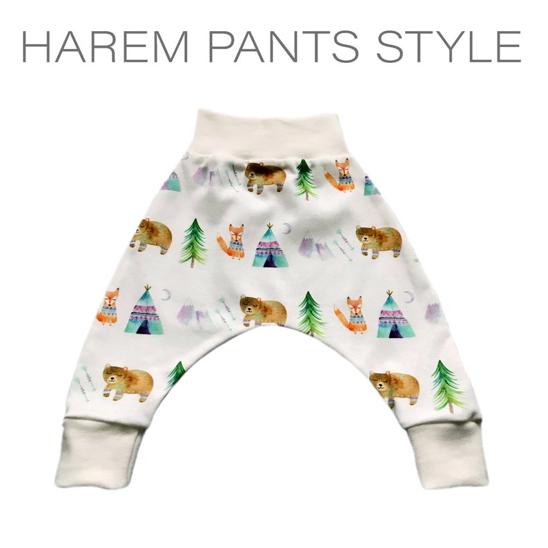 May include: White harem pants with a whimsical woodland print featuring bears, foxes, and teepees. The print is in shades of blue, green, orange, and purple.