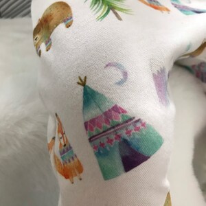 May include: White fabric with a repeating pattern of colorful teepees, bears, foxes, and crescent moons. The fabric has a soft, textured feel.