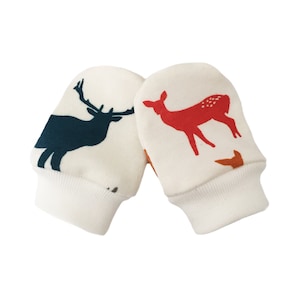May include: A pair of white baby mittens with a deer and elk print. The mittens have a white cuff.