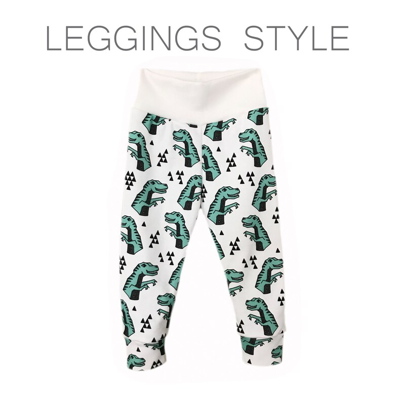 May include: White leggings with a green dinosaur print. The dinosaurs are outlined in black and have a white background. The leggings have a white waistband.