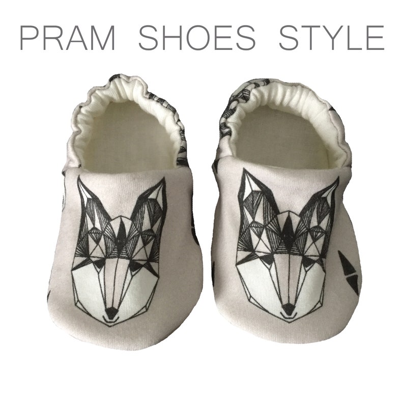 May include: A pair of baby shoes with a geometric fox design in black and white on a light gray background. The shoes have a white elastic band around the top.