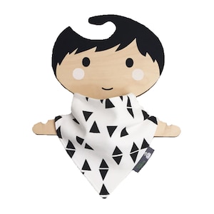 Puede incluir: Colgador de madera para muñecas con un pañuelo de patrón geométrico blanco y negro. La muñeca tiene el pelo negro y una cara sonriente.