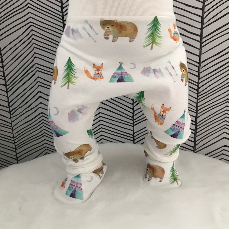 May include: White baby leggings with a woodland animal print featuring bears, foxes, and teepees. The leggings have a gathered elastic waistband and are made of a soft, stretchy fabric.
