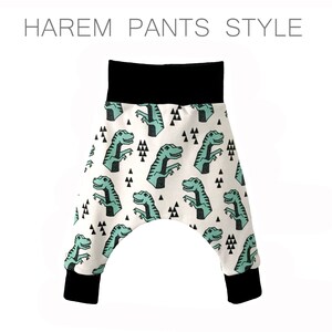 May include: White harem pants with a black waistband and black cuffs. The pants have a repeating pattern of green dinosaurs and black triangles.