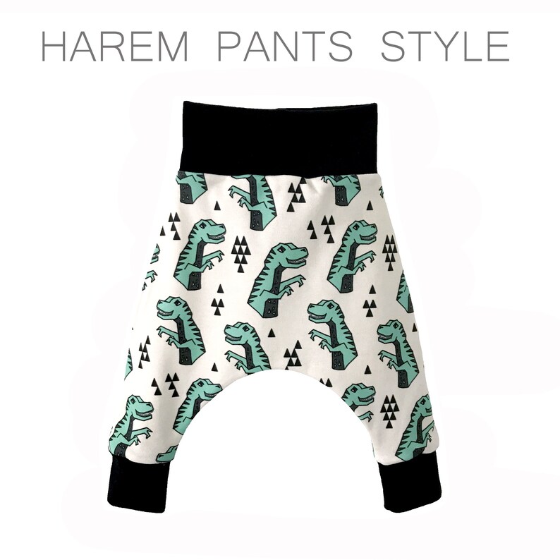 May include: White harem pants with a black waistband and black cuffs. The pants have a repeating pattern of green dinosaurs and black triangles.