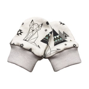 May include: A pair of baby mittens with a geometric fox and mountain design. The mittens are white with black and teal accents, and gray ribbed cuffs. The design features geometric shapes and patterns.