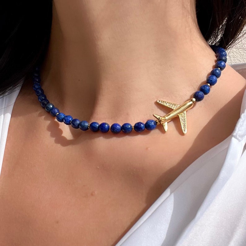 May include: A gold airplane charm hangs from a necklace made of dark blue lapis lazuli beads.