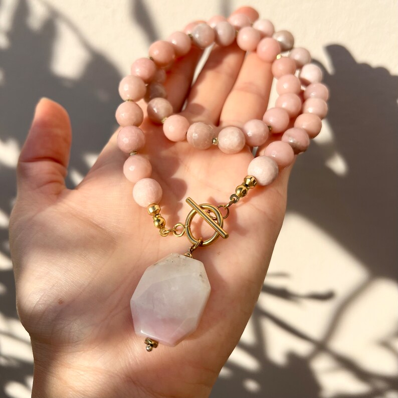 May include: A pink gemstone necklace with a large, faceted, pink gemstone pendant. The necklace has a gold toggle clasp.
