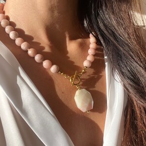 May include: A gold necklace with a large, faceted, pink and white gemstone pendant. The necklace is made of small, pink beads.