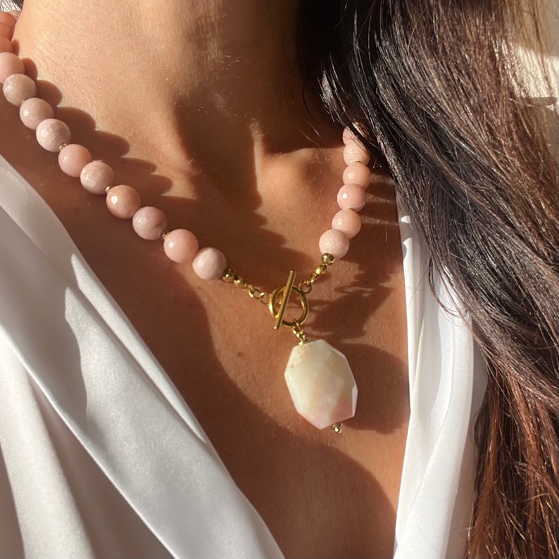 May include: A gold necklace with a large, faceted, pink and white gemstone pendant. The necklace is made of small, pink beads.