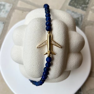 May include: A blue lapis lazuli beaded bracelet with a gold airplane charm. The airplane has clear crystal accents.