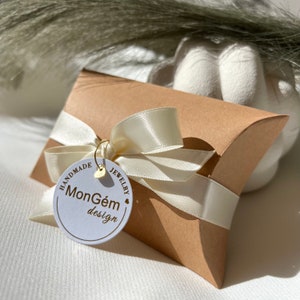 May include: A brown cardboard pillow box with a white satin ribbon and a white circular tag that says "Handmade Jewellery MonG&eacute;m design".