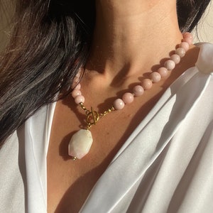 May include: A pink gemstone necklace with a large, white, faceted gemstone pendant. The necklace is made of small, round beads and has a gold clasp.