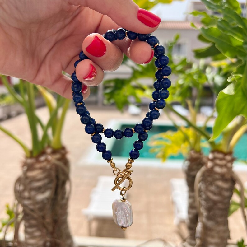 May include: A dark blue beaded bracelet with a gold toggle clasp and a white pearl pendant.
