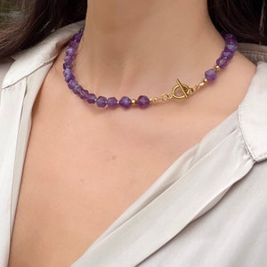 May include: A gold chain necklace with a toggle clasp and purple amethyst beads.