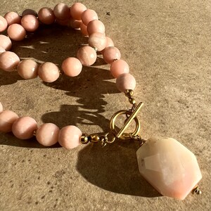 May include: A pink opal gemstone necklace with a large, faceted pendant and a gold toggle clasp.