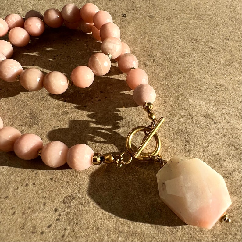 May include: A pink opal gemstone necklace with a large, faceted pendant and a gold toggle clasp.
