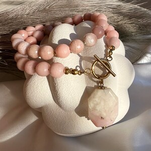 May include: A double-strand pink gemstone necklace with a large, faceted pink gemstone pendant and a gold toggle clasp.