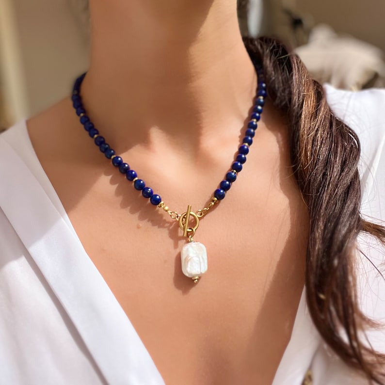 May include: A gold chain necklace with a large white baroque pearl pendant. The chain is made of small blue beads.