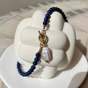 May include: A blue lapis lazuli beaded bracelet with a gold toggle clasp and a large white pearl charm.