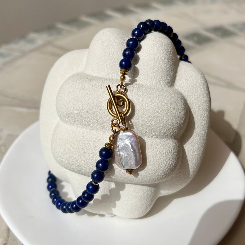 May include: A blue lapis lazuli beaded bracelet with a gold toggle clasp and a large white pearl charm.