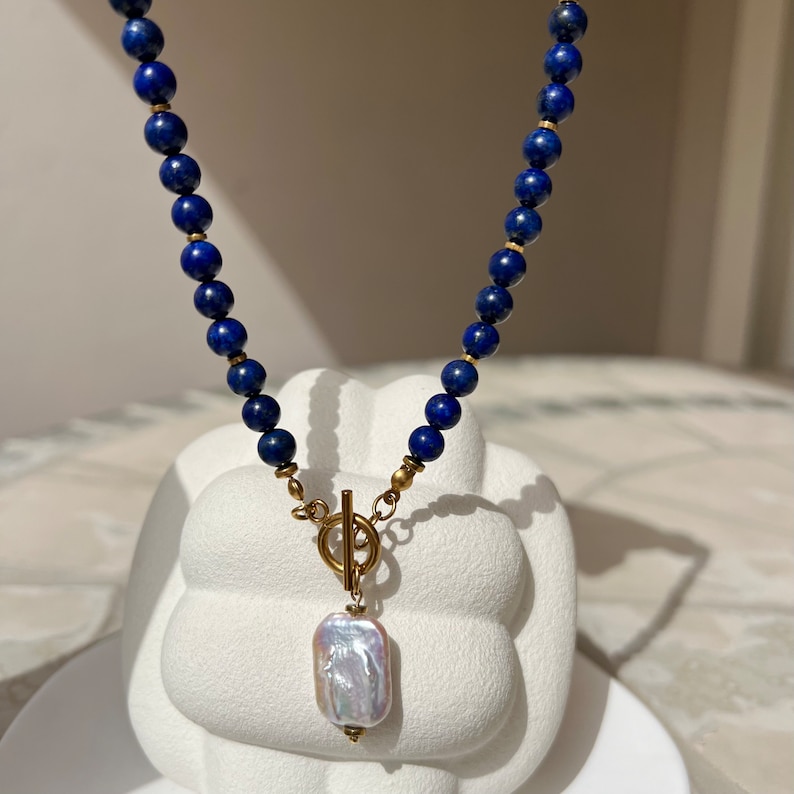 May include: A gold necklace with a large, white pearl pendant. The necklace is made of dark blue beads.