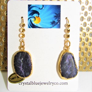 May include: Gold dangle earrings with a purple and black stone pendant. The earrings have a gold chain with small gold beads.