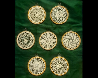 Puede incluir: Ocho doilies de ganchillo blanco en aros de madera, dispuestos sobre un fondo verde.