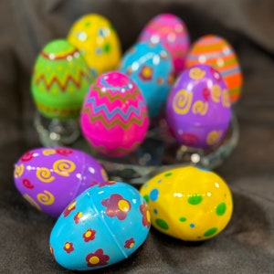 May include: A collection of colourful Easter eggs with various patterns, including swirls, zigzags, flowers, and polka dots. The eggs are arranged on a clear glass plate.