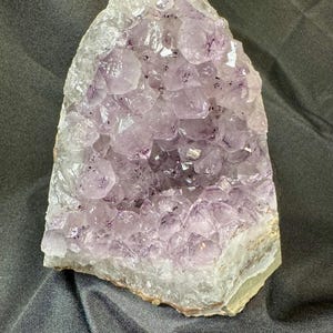 May include: A large amethyst geode with a cluster of purple crystals. The geode is partially open, revealing the crystals inside. The geode is on a dark grey background.