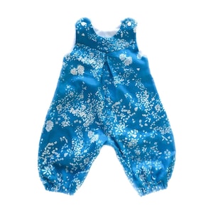 May include: A blue baby romper with a white floral pattern. The romper has straps and a gathered waist.