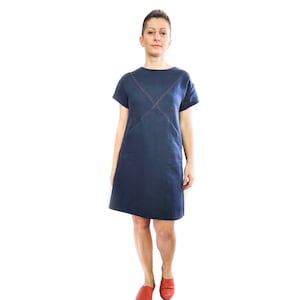 May include: A navy blue linen dress with short sleeves and a contrasting red stitch detail. The dress has a simple, straight silhouette and a slightly rounded neckline.