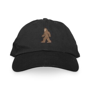 May include: A black baseball cap with an embroidered brown Bigfoot graphic.