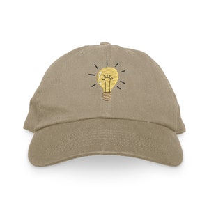 May include: A khaki baseball cap with an embroidered lightbulb design. The lightbulb is yellow with a black outline and a brown base.