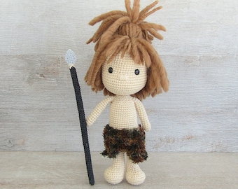 May include: A handmade crochet doll depicting a cave dweller. The doll has a light tan body, brown hair, and a fur skirt. It holds a black spear with a gray tip. The doll is approximately 8 inches tall.
