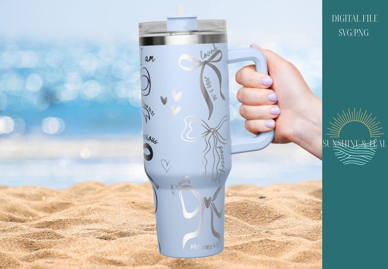 Puede incluir: Un vaso t&eacute;rmico azul claro con asa, decorado con lazos plateados, corazones y escritura. El vaso tiene una tapa transparente y se sostiene en una playa de arena con el oc&eacute;ano al fondo. El texto incluye "amado" y "poderoso".