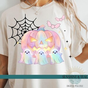 Może przedstawiać: Kremowa koszulka z motywem Halloween. Projekt zawiera pastelową dynię, trzy pastelowe duszki, różowe nietoperze, czarną pajęczynę i gwiazdy. Tekst "SUNSHINE & TEAL" i "DIGITAL PNG FILE" znajduje się na dole.