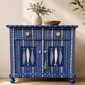 May include: A rectangular blue cabinet featuring two drawers and two doors with vertical stripes and small white rectangular accents. The doors display painted fish motifs in gold and light blue. The cabinet has round knobs and a small grey tassel.