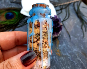 May include: A small glass bottle with a cork stopper is filled with dried herbs and crystals. The bottle is sealed with blue wax that has dripped down the sides.