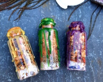 May include: Three small glass bottles with cork stoppers filled with dried herbs and crystals. The bottles are sealed with wax that has dripped down the sides. The wax is green, purple, and yellow.